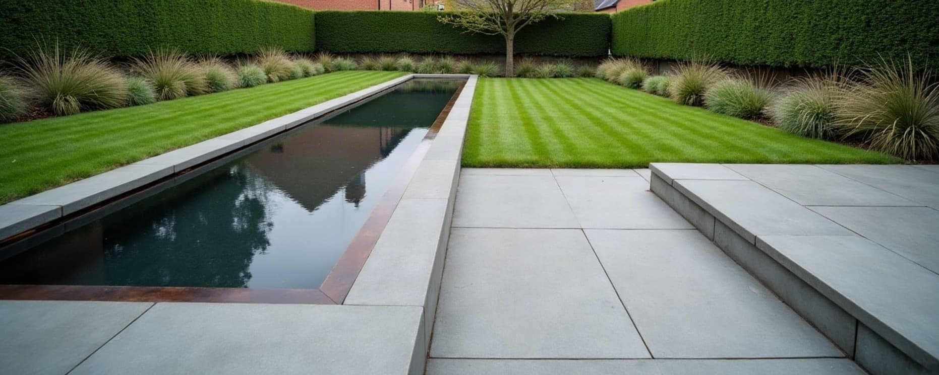 Jardin de particulier terminé : terrasse en pierre bleue, bassin miroir à rive corten, pelouse tondue et haie taillée